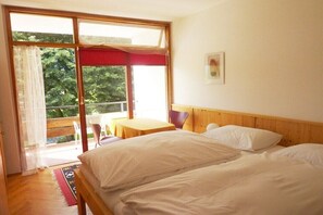 A room with a bed, a table, and a chair. There is a balcony with a view of trees. - Holiday apartment with 2 bedrooms (Steindorf)