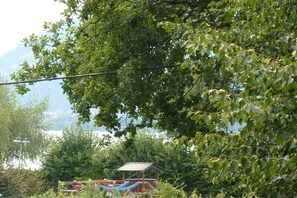 Une aire de jeux avec des toboggans et un petit abri, entourée d’arbres et offrant une vue sur un plan d’eau.