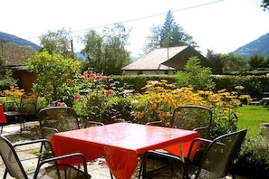 An outdoor seating area with tables and chairs, surrounded by a garden with various plants and flowers. - Holiday apartment with 2 bedrooms (Steindorf)