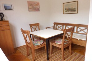 Ein kleiner Essbereich mit einem Tisch, vier Stühlen, einem Holzschrank und einem gemusterten Teppich.