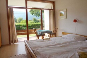 A bedroom with a bed, a table, and chairs, a window with curtains, and a view of greenery. - Holiday apartment with 2 bedrooms (Steindorf)