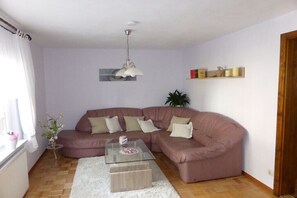 A living room with a sectional sofa, a glass coffee table, a white rug, a pendant light, and a plant. - Holiday home with 1 bedroom (Katzhütte)