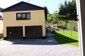 A two-story building with a garage, a paved driveway, and a well-maintained lawn with trimmed bushes and trees. - Holiday home with 1 bedroom (Katzhütte)
