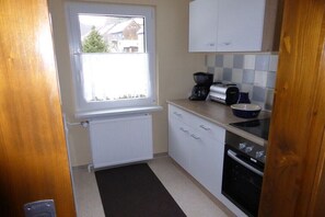 A compact kitchen with a window, white cabinets, a black stove, and a coffee maker. - Holiday home with 1 bedroom (Katzhütte)