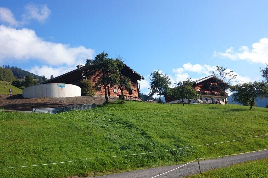 Een landelijke omgeving met een grote, cilindervormige constructie, een houten gebouw met een schuine kap en een kleiner gebouw met een rood dak.