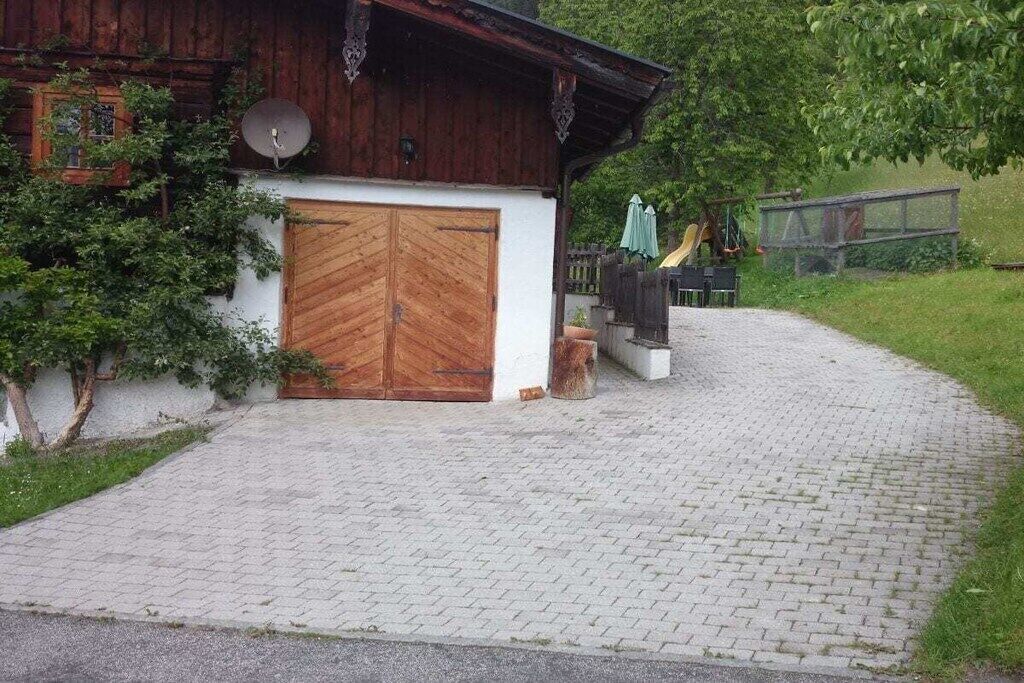 A rustic wooden building with a double wooden door, a satellite dish, and a paved driveway leading to a covered outdoor area.