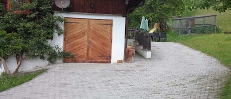 A rustic wooden building with a double wooden door, a satellite dish, and a paved driveway leading to a covered outdoor area.