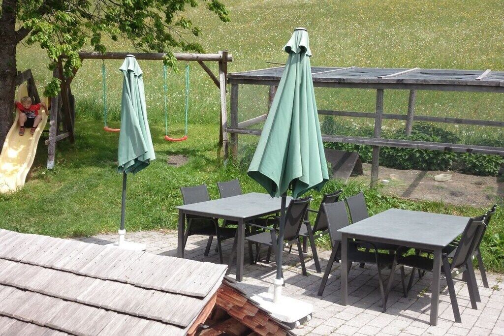 Un espace extérieur aménagé en patio, avec des tables et des chaises, une clôture en bois et une balançoire.