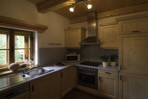 A kitchen with wooden cabinets, a microwave, a sink, and a stove. - Holiday apartment with 1 bedroom (Rauris)