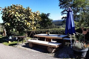 Juego de mesa y banco de madera al aire libre, con una sombrilla azul, rodeado de grava y follaje.