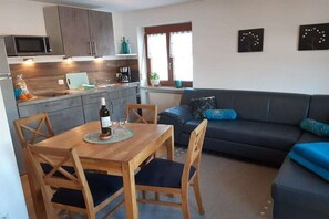 A compact living space with a dining table, chairs, a sofa, and a kitchenette. - "Stoffelberg" in the Seeblick House (Niedersonthofen)