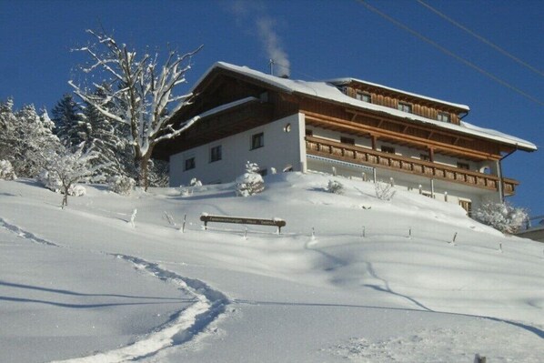 Un chalet de dos plantas con fachada de madera, ubicado en una ladera nevada.