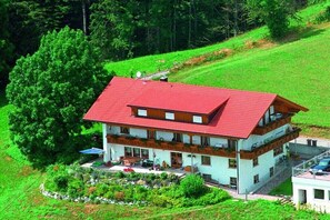 A multi-story building with a red roof, surrounded by lush greenery and trees. - "Stoffelberg" in the Seeblick House (Niedersonthofen)