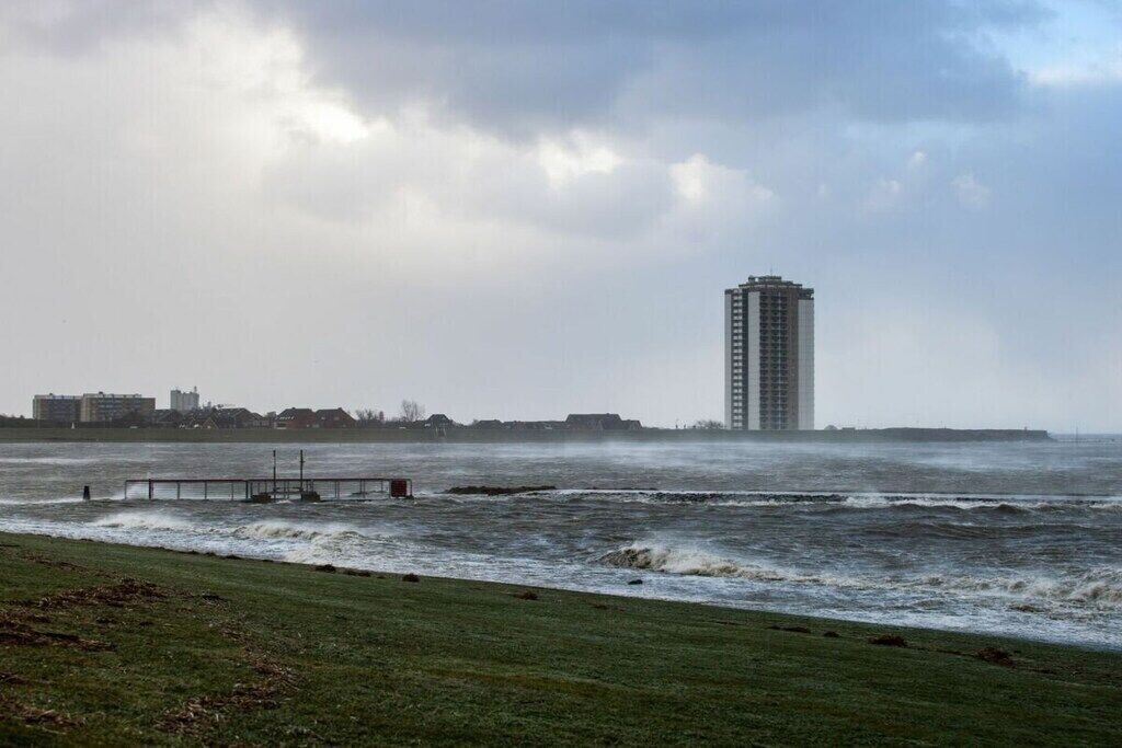 En kustutsikt med en hög byggnad, en pir och ett grönområde.
