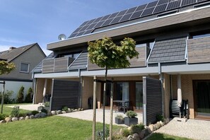 Una moderna casa a due piani con pannelli solari, un patio coperto e un giardino curato.
