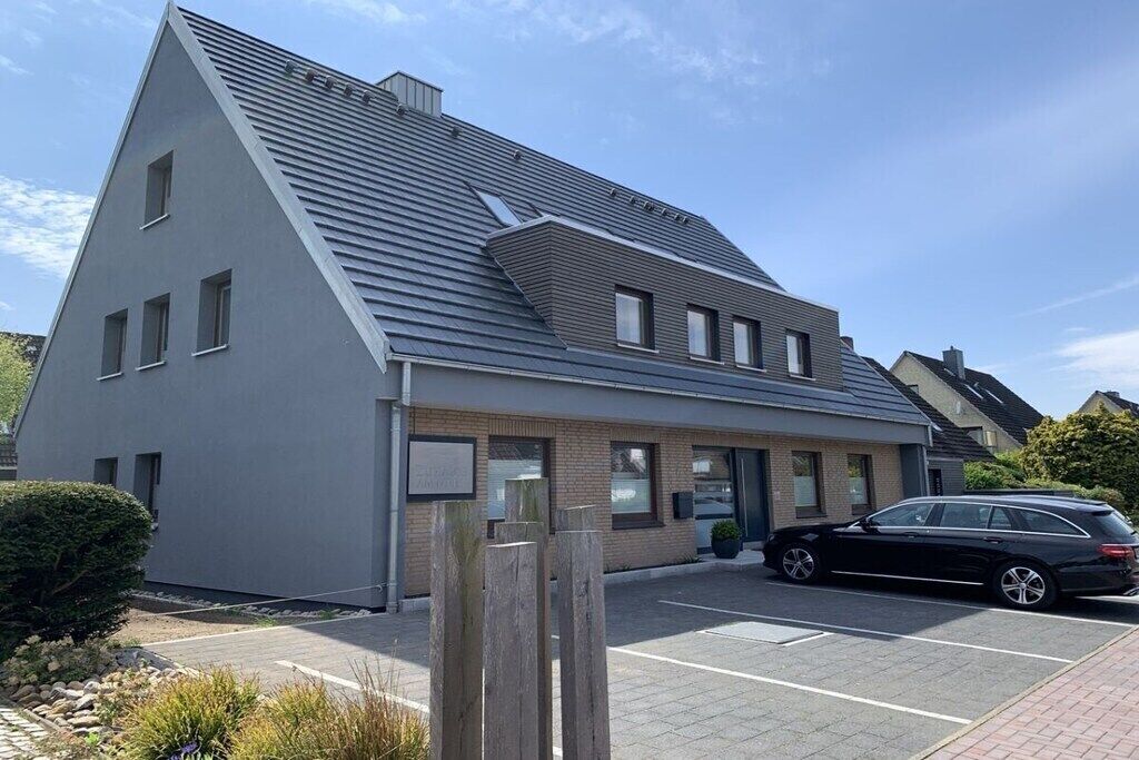 Un bâtiment moderne doté d’un toit en pente, d’un parking et d’une voiture noire garée devant.