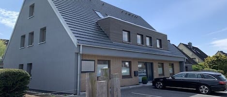 A modern building with a sloped roof, a parking lot, and a black car parked in front.