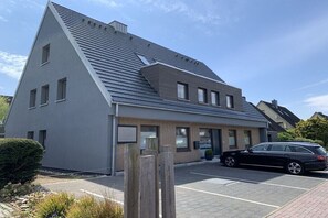 Ein modernes Gebäude mit geneigtem Dach, einem Parkplatz und einem schwarzen Auto davor.