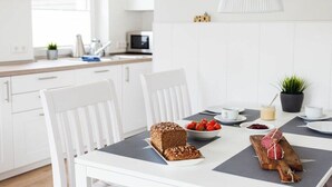 A modern kitchen with white cabinetry, a dining table with a loaf of bread, strawberries, and a wooden board with a wrapped item. - TRINCHEN in the home by the sea (Büsum)