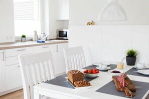 Una cucina moderna con mobili bianchi, un tavolo da pranzo con una pagnotta, fragole e un tagliere con un oggetto avvolto.