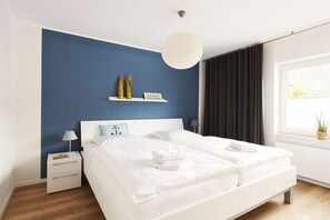Camera da letto moderna con un letto grande, comodini, una lampada a sospensione e una finestra con tende.