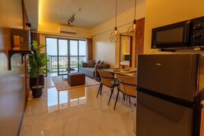 A modern kitchen with a refrigerator, a dining area with a table and chairs, a sofa, and a large window with a view.