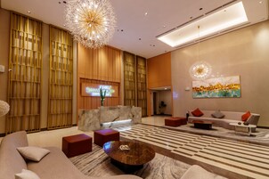 Un moderno vestíbulo de hotel con mostrador de recepción, área de descanso e iluminación decorativa.