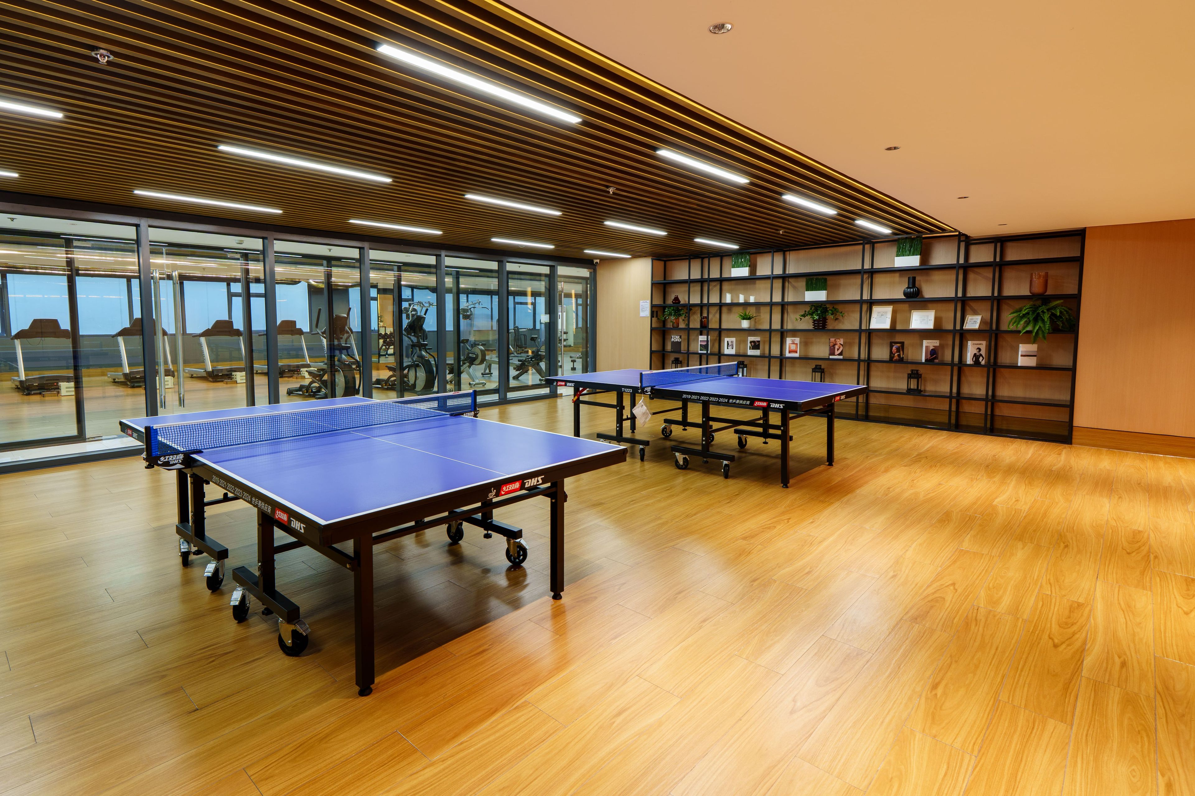 A spacious room with two ping pong tables, large windows, and a wall with shelves displaying framed items.