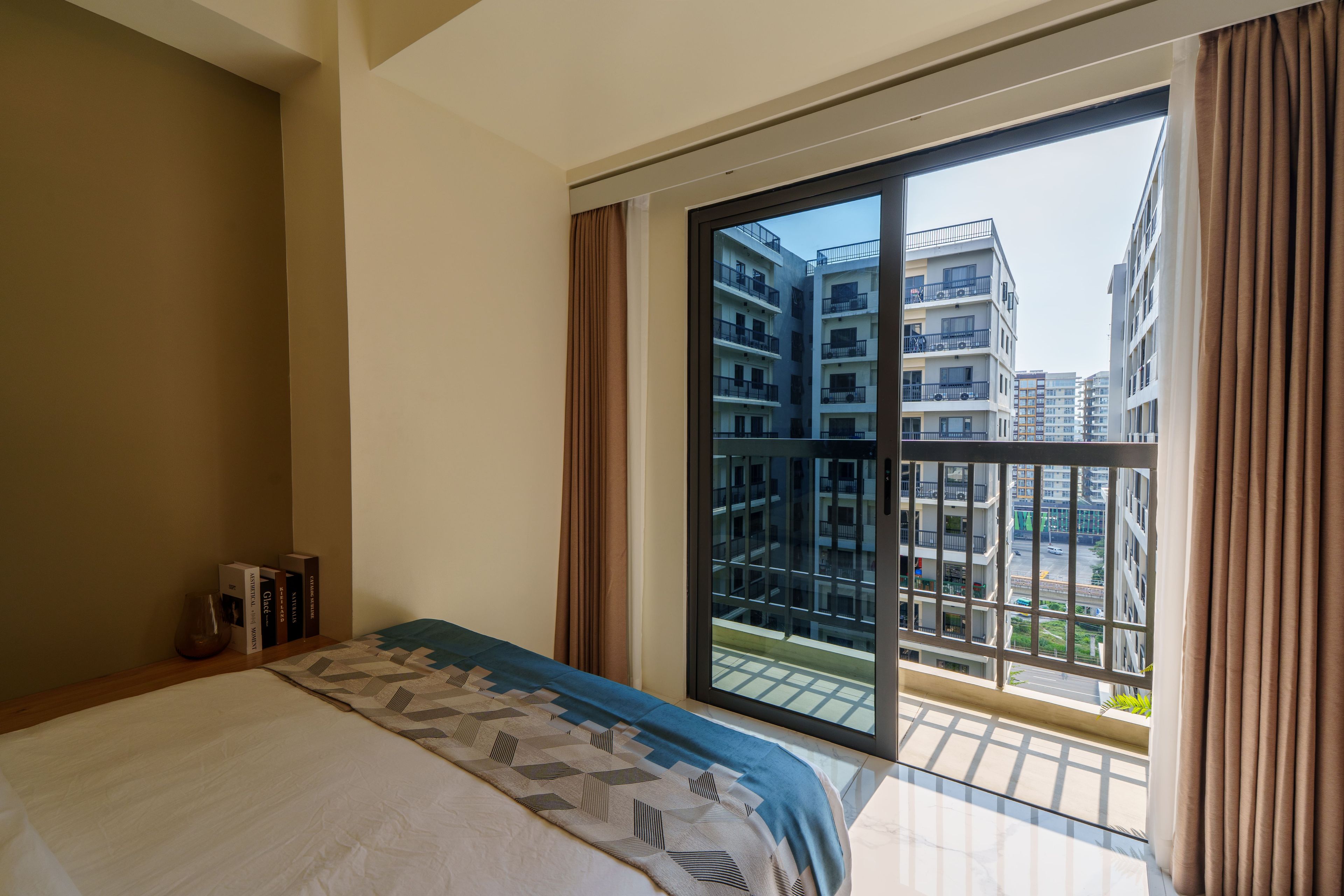 Une chambre d’hôtel avec une grande fenêtre, un lit et une petite table sur laquelle sont posés des livres.