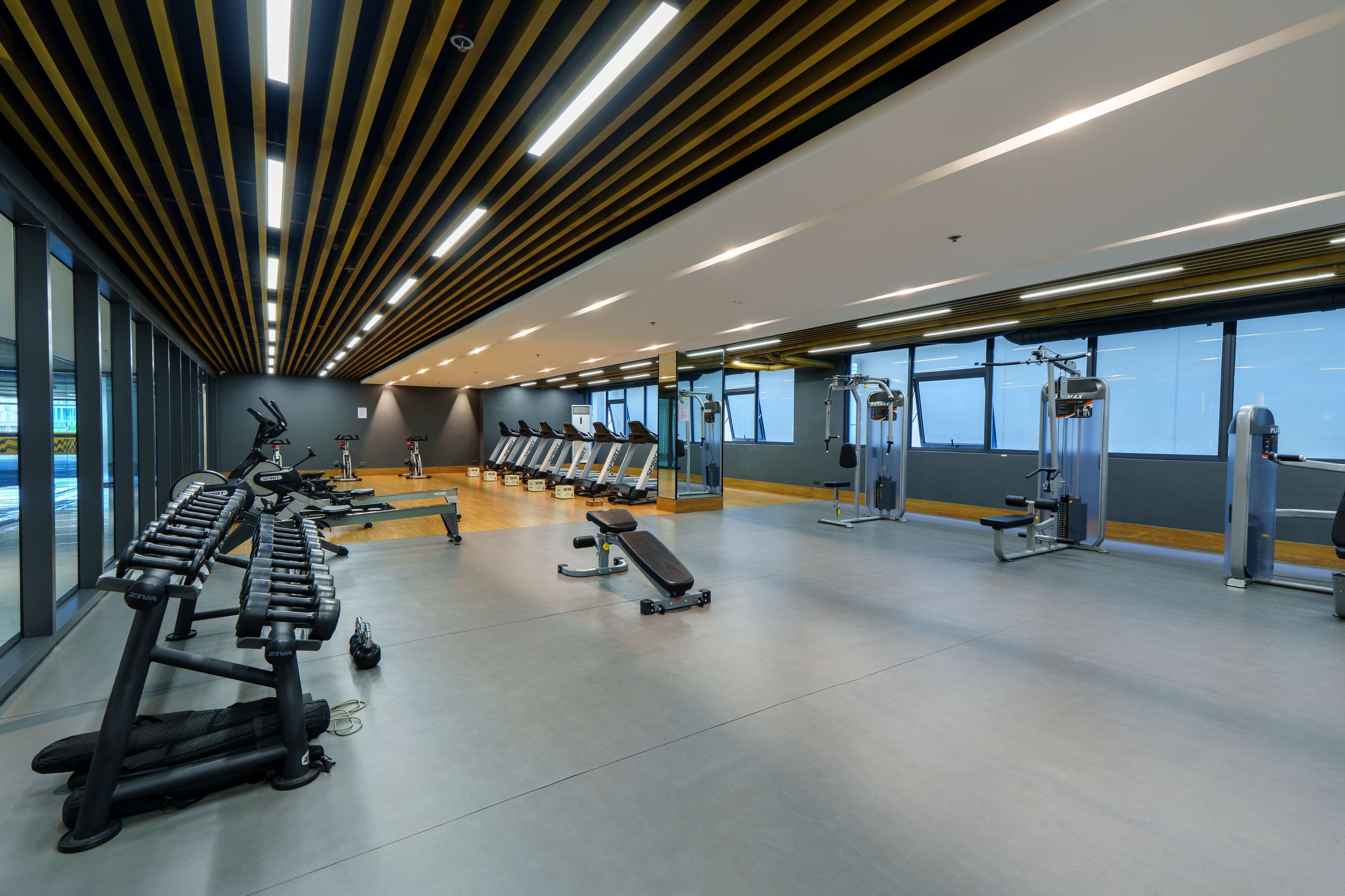 A gym with various exercise equipment, large windows, and a modern ceiling design.