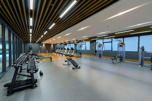 Une salle de sport équipée de divers appareils d’exercice, dotée de grandes fenêtres et d’un design moderne au niveau du plafond.