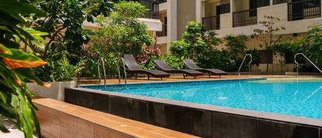 Une piscine avec des chaises longues et vue sur un immeuble à plusieurs étages.
