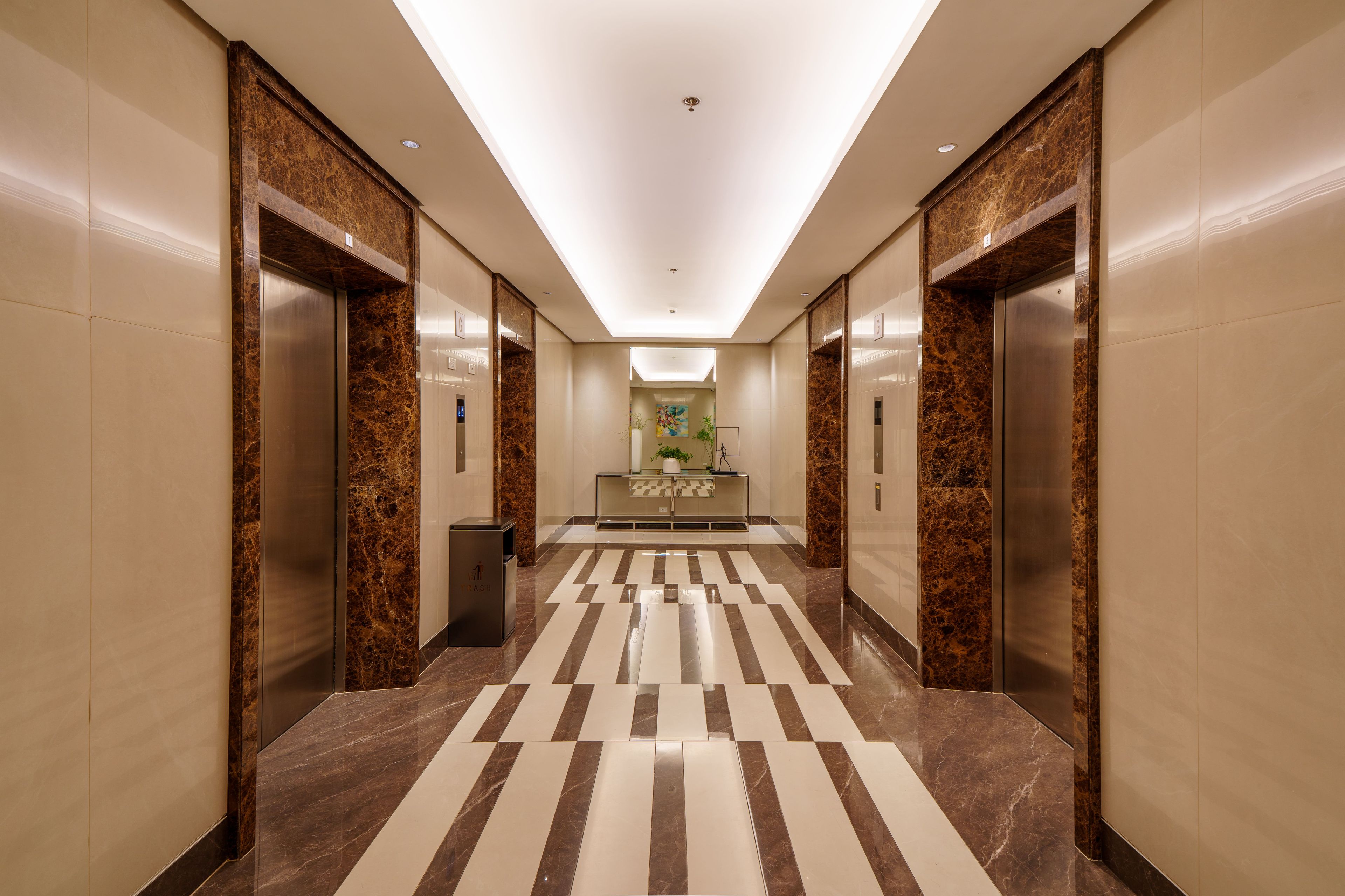 A modern hotel lobby with a marble floor, elevators, and a reception desk.