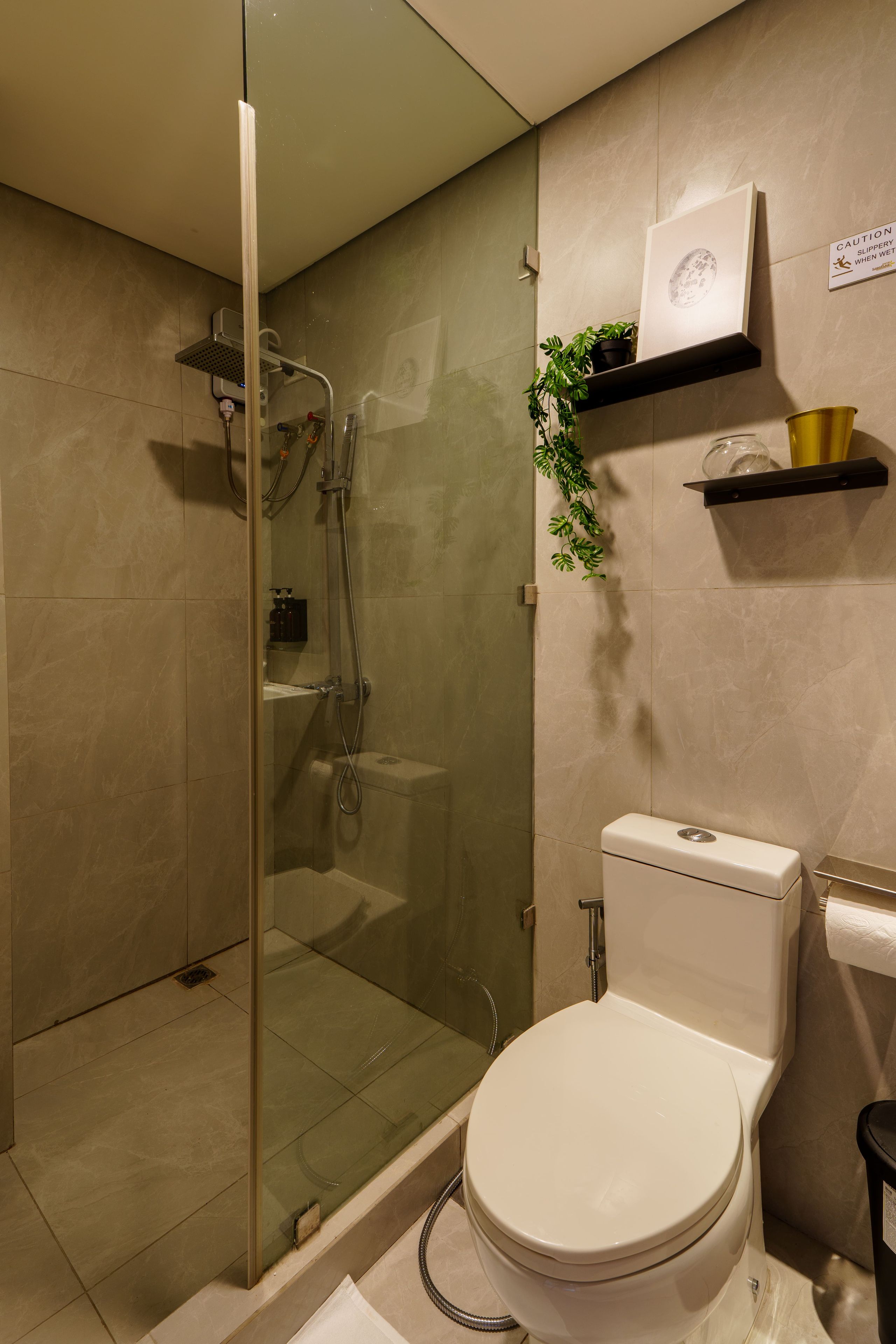 Une salle de bain moderne avec une douche en verre, des toilettes et une étagère sur laquelle est posée une plante en pot.