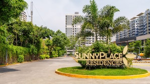 A residential area with a sign for SunnyPlace Residences, surrounded by greenery and modern buildings. - SunnyPlace (Parañaque)
