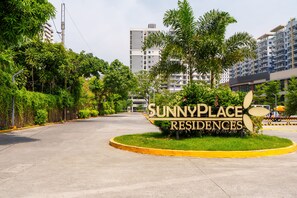 Zona residencial con un letrero que indica SunnyPlace Residences, rodeada de vegetación y edificios modernos.