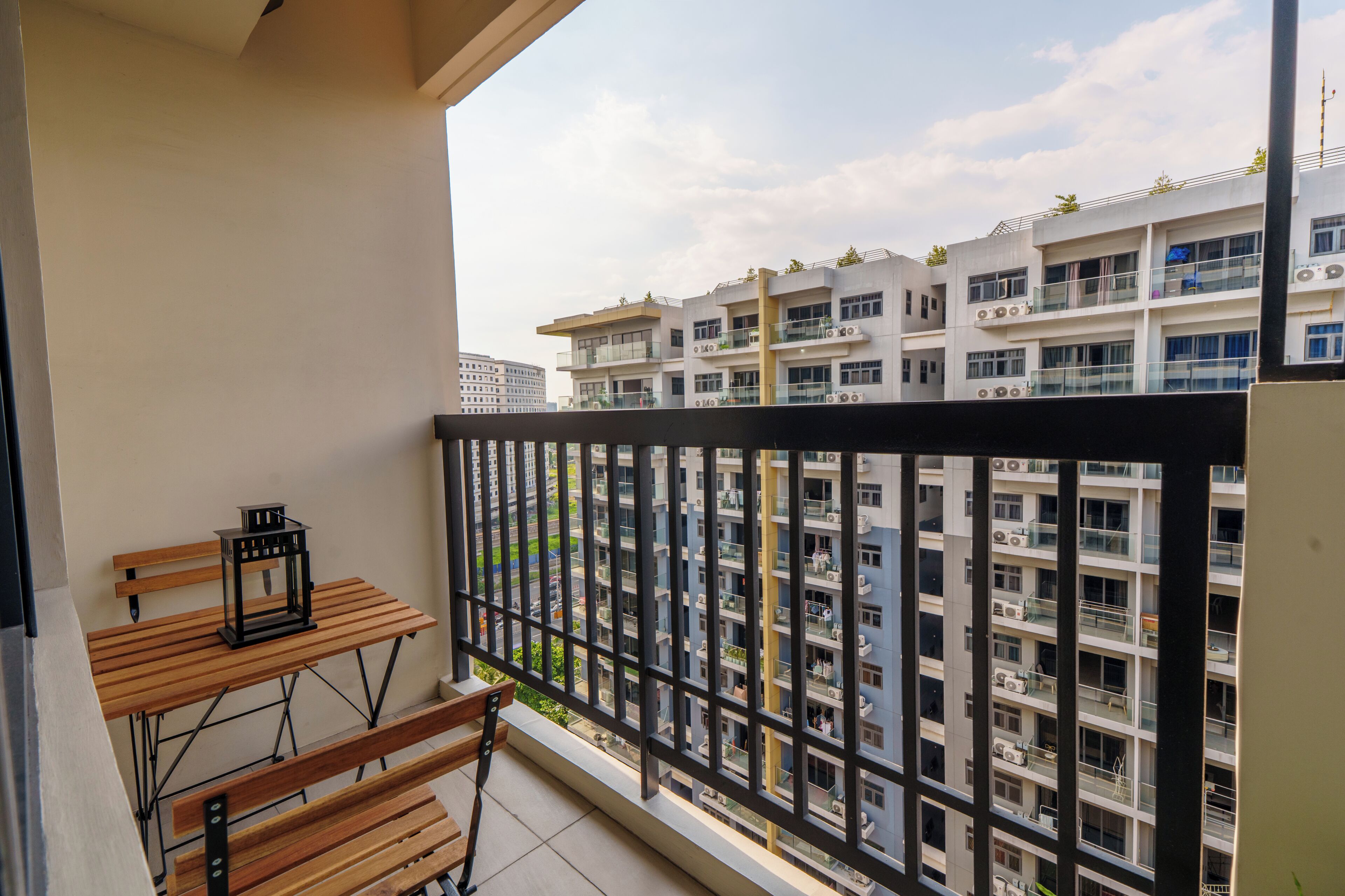 A balcony with a wooden bench and a lantern, overlooking a multi-story residential building with balconies.