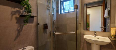 Un baño moderno con ducha envuelta en vidrio, un lavamanos blanco y un ventanal que proporciona luz natural.