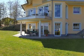 Un edificio residencial de varios pisos con un balcón, un patio con muebles de exterior y un césped bien cuidado.