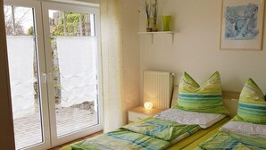 Um quarto com cama, mesa de cabeceira com luminária, radiador, janela com cortinas e prateleira com objetos decorativos.