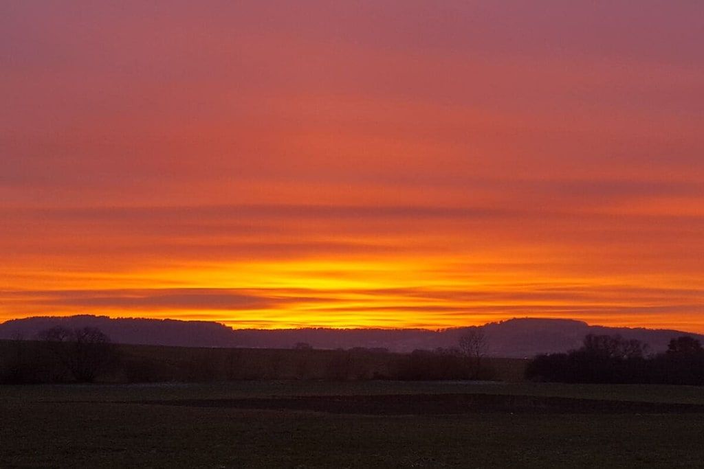 A sunset over a flat landscape with a distant hill.