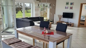Uma sala de estar moderna com uma mesa de jantar, bancos acolchoados, um sofá e uma televisão.