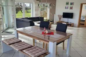 Una sala de estar moderna con una mesa de comedor, bancos acolchados, un sofá y un televisor.