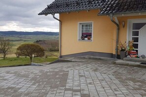Un bâtiment avec un toit recouvert de tuiles, une fenêtre offrant une belle vue et une zone d’entrée pavée.