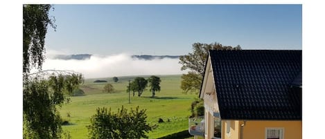 A house with a balcony overlooking a green field and a misty landscape.