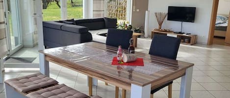 A modern living room with a dining table, cushioned benches, a sofa, and a television.