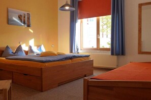 A bedroom with a bed, a window with curtains, a radiator, and a painting on the wall. - A1 in the apartment building near Müritz (Waren (Müritz))