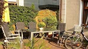 Eine Terrasse im Freien mit Tisch und Stühlen, umgeben von Pflanzen und einem Fahrrad.