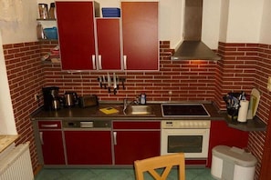 A compact kitchen with red cabinets, a sink, stove, and a trash can. - A1 in the apartment building near Müritz (Waren (Müritz))
