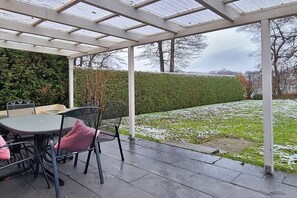 A covered patio with a table and chairs, a hedge, and a view of a grassy area. - Holiday home with 2 bedrooms (Klein Labenz)
